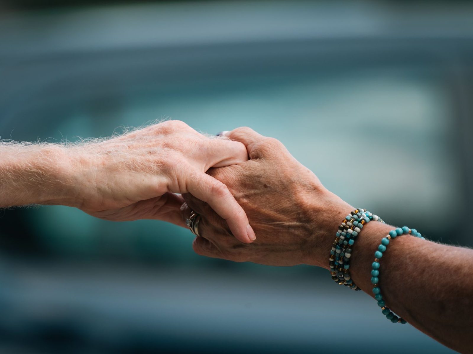A younger person's hand resting supportively on an older person's hand