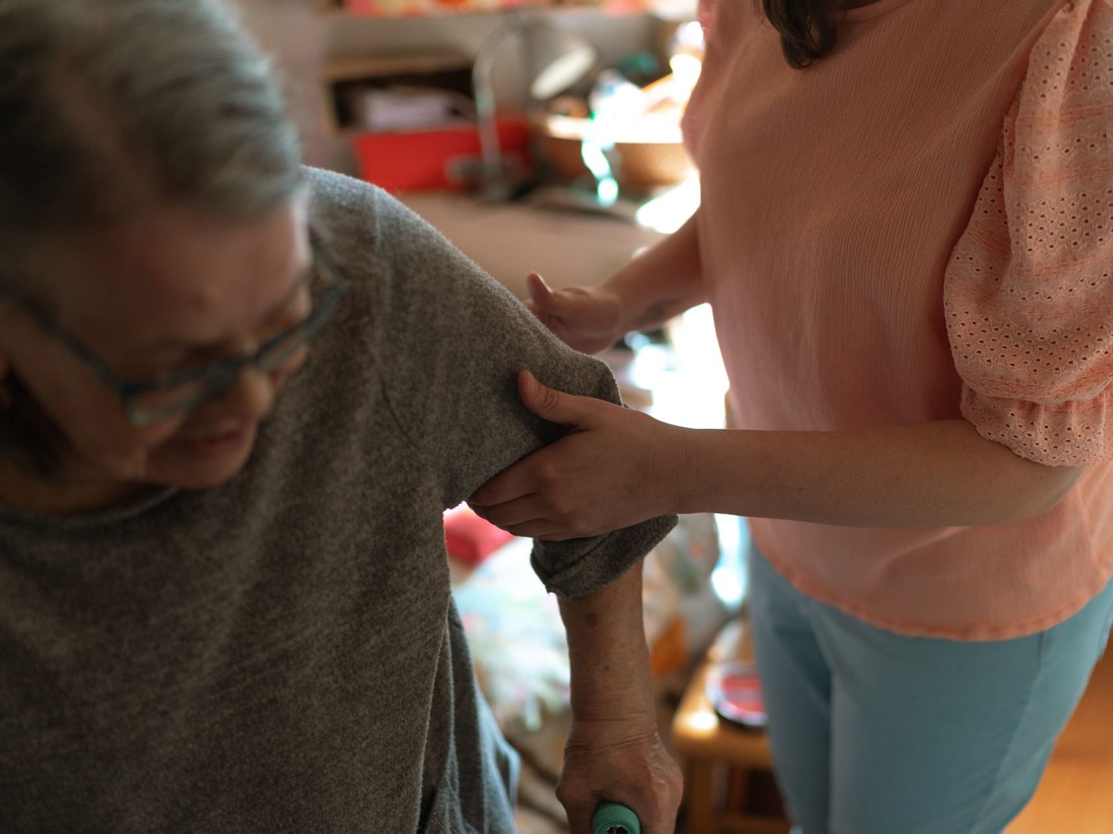 A carer helping an older person put on a cardigan at home