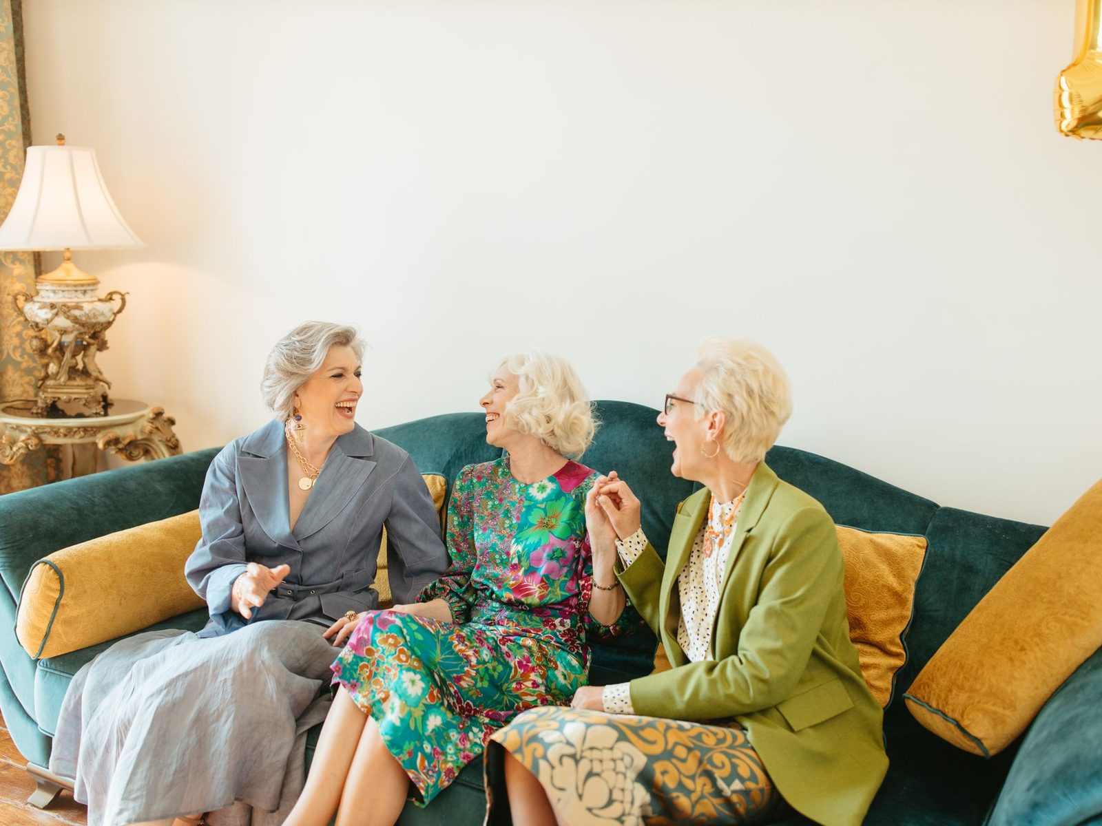 Three older women sitting together on a sofa at home, talking